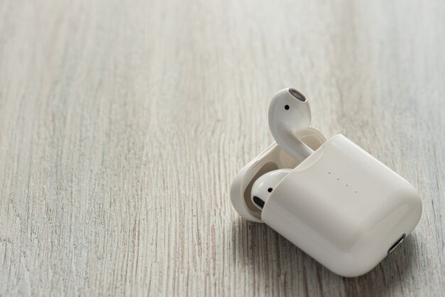 White wireless headphones in a charging case on a wooden table.