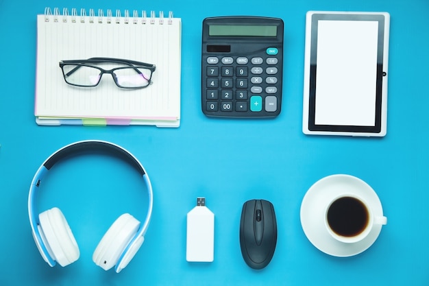 White wireless headphones, glasses, coffee and other objects on the blue background.