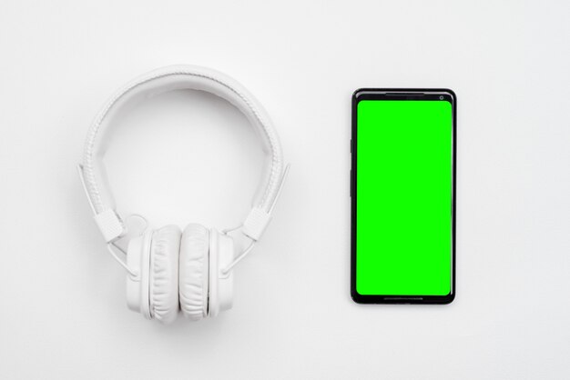 White wireless headphones and phone with green screen isolated on a white background.