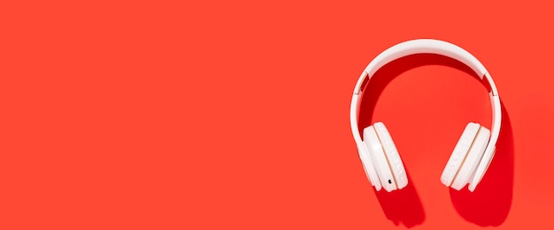 White wireless headphones on a red background Top view flat lay Banner