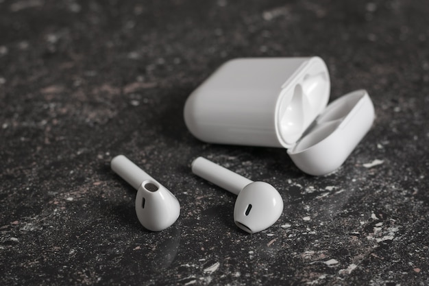 White wireless headphones with charging case on black stone background. Modern wireless accessories.