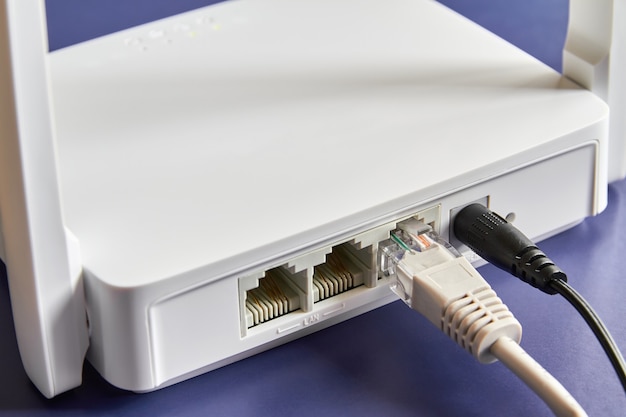 White wireless router on blue background connected by cable to the Internet