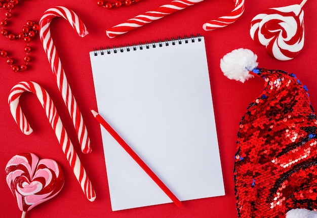 White wish list blank with candies and santa hat on red background