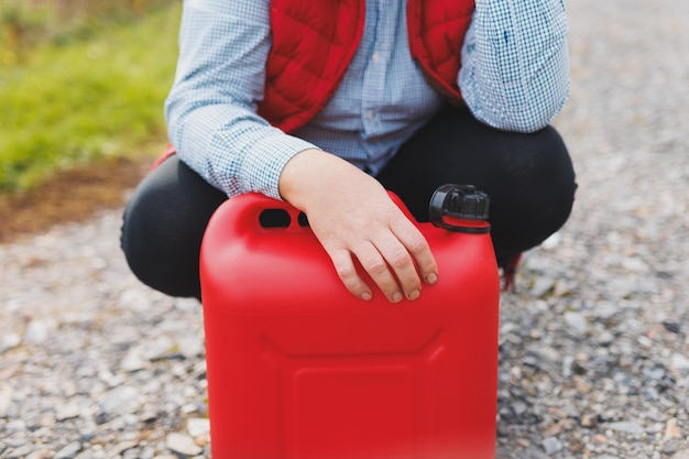 White woman in red vest holding red gasoline container and posing on scenic nature country road