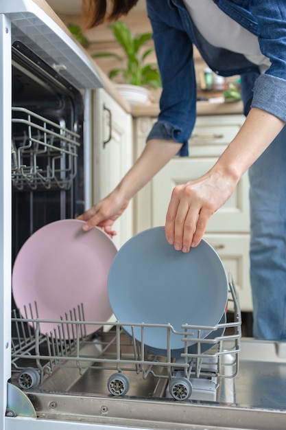 Белая женщина, моющая посуду вручную или загружающая ее в посудомоечную машину для мытья посуды по дому.