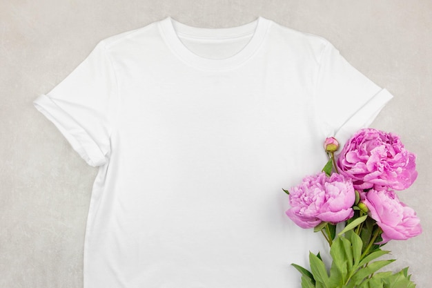 灰色のコンクリートの背景にピンクの牡丹の花と白い女性の綿のTシャツのモックアップデザインTシャツテンプレート印刷プレゼンテーションモックアップ上面図フラットレイ