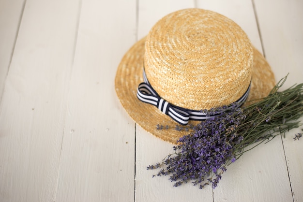 on white wood lies a straw hat with a bow and a freshly plucked field fragrant bouquet of lavender.