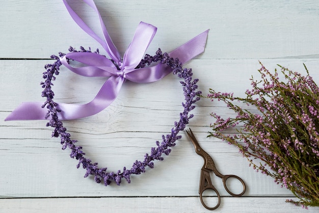 on a white wooden background purple heart made of purple flowers, scissors and a heather b