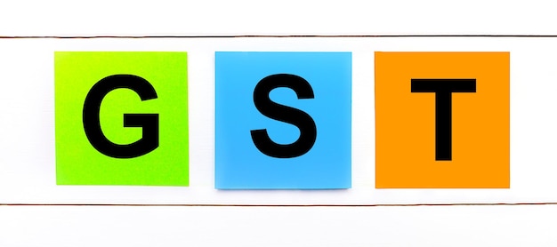 On a white wooden background there are three colorful bright stickers with text GST Goods and Services Tax