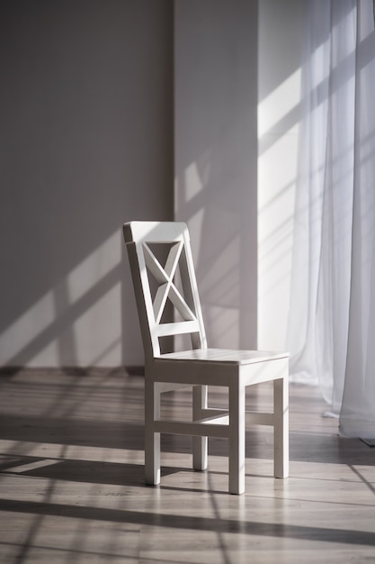 White wooden chair against the background of a beautiful bright spacious room with white walls and light parquet in the morning sun