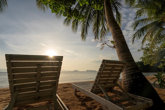 태국 코 야오 노이(Koh Yao Noi)의 일출 하늘이 있는 모래 해변에 있는 흰색 나무 의자