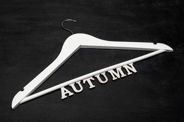 Фото Белая деревянная вешалка для пальто и надпись осень на черном фоне. осенняя концепция коллекции одежды.