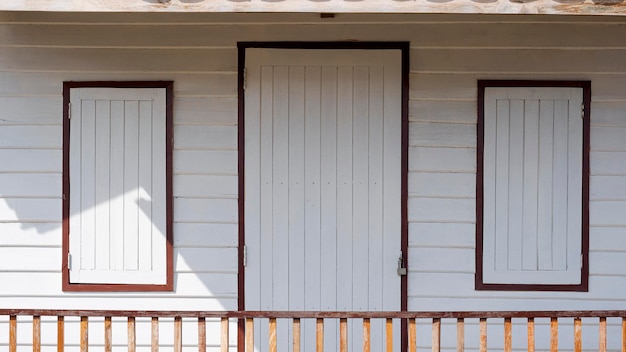 White wooden door and windows with porch railing made from\
recycled old wood panels