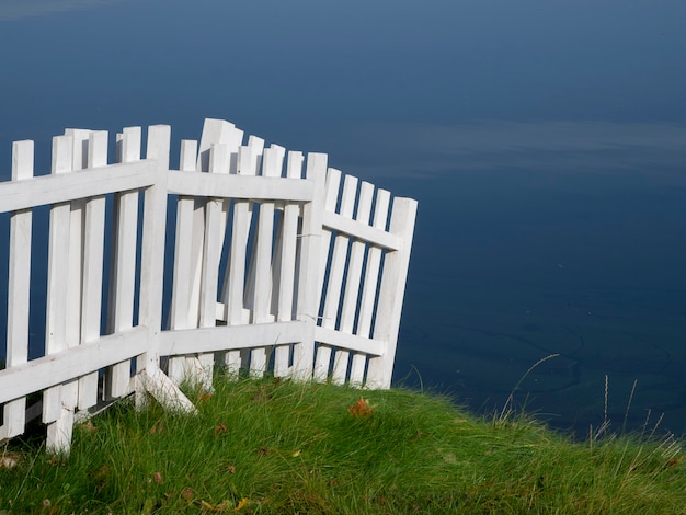 White wooden fence with green lawn and water.