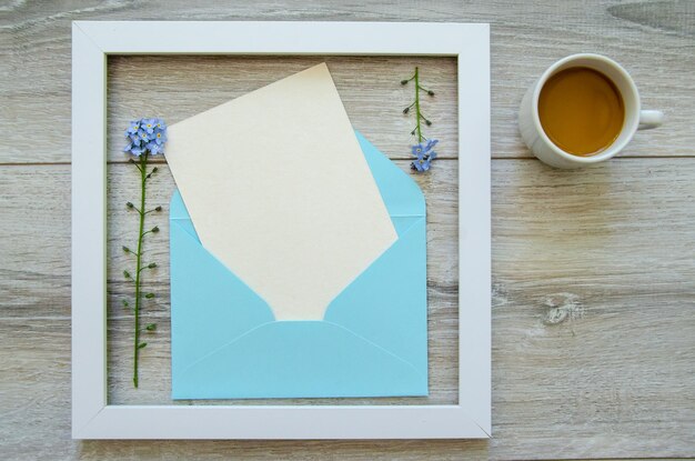 白い木製のフレームと青い封筒 白いポストカードのコピースペース 小さな青い花
