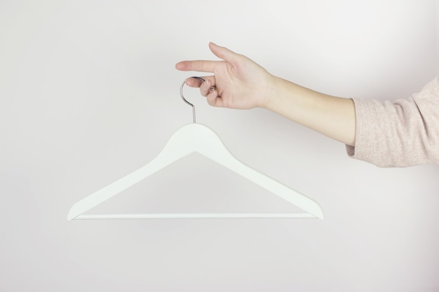 Photo white wooden hanger in female hands against  light wall. store concept, sale, design empty hangers