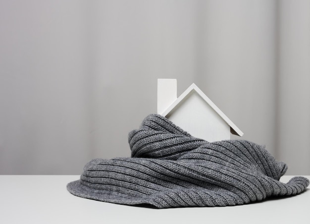 White wooden miniature house wrapped in a gray knitted scarf. Building insulation concept, loans for repairs