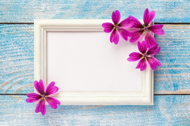 Portafoto in legno bianco con fiori viola su fondo di carta rosa.