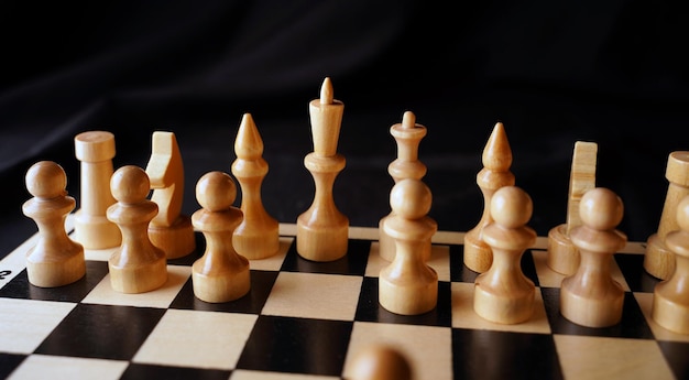 Белые деревянные фигуры на шахматной доске Шахматная доска во время игры на черном фоне