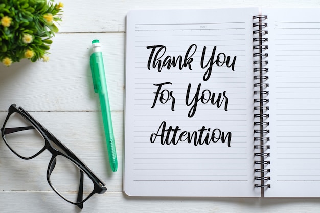 White wooden table with eyeglasses, pen, decorative plants, and notebook written with Thank You For Your Attention. Top view with copy space, flat lay.