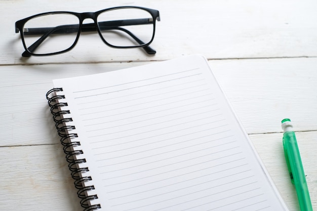 White wooden table with note book, eyeglasses, pen, decorative plants. Top view with copy space, flat lay.