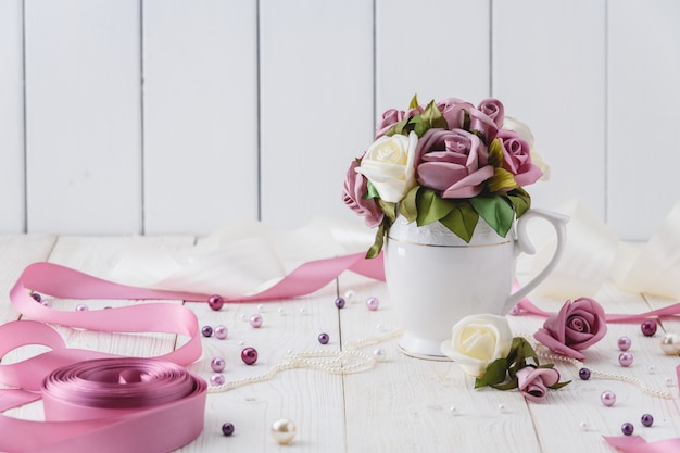 White wooden table with pink flowers, ribbons and beads. Wedding style