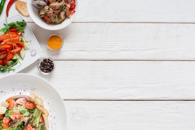 White wooden table with warm salads free space. Top view on kitchen desk with meat side dishes, flat