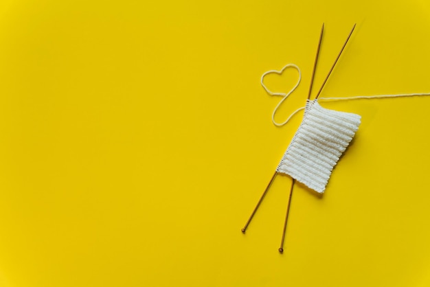 Photo white wool knitting needles and a piece of knitting against a yellow background