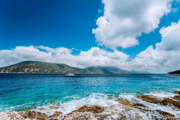 White yacht drift in middle of open crystal clear emerald green sea water near Fiskardo town Ithaki Island in background Amazing white cloudscape in blue sky Kefalonia Ionian islands Greece