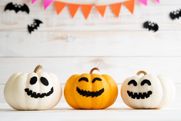 White and yellow ghost pumpkins on white wooden board background with bat. 