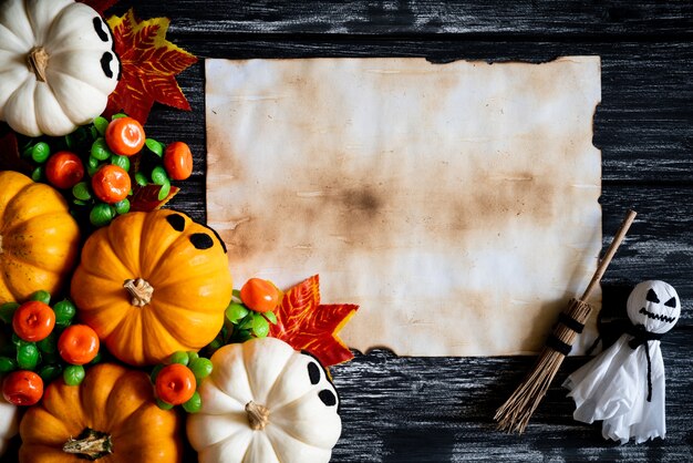 White and yellow ghost pumpkins with Autumn leaves and old paper on a black wooden backgro