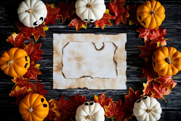 木製のテーブルbackgrounに秋の葉と古い紙と白と黄色のゴーストカボチャ