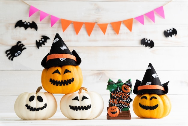White and yellow ghost pumpkins with witch hat on white wooden board background with bat. 