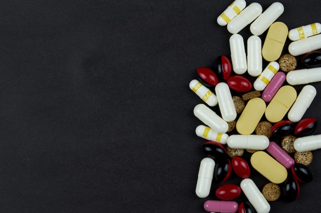 White and yellow pills, tablets, vitamins, medicine, pills and drugs scattered on a dark table. Pills for treatment and medicine.