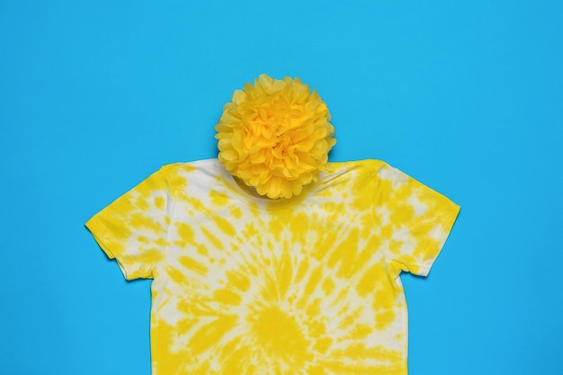 A white and yellow tie dye Tshirt and a large paper pompom on a blue background Flat lay