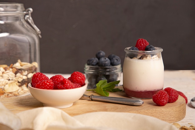 white yogurt with fresh raspberries and blueberries on the serving board on the rustic table.