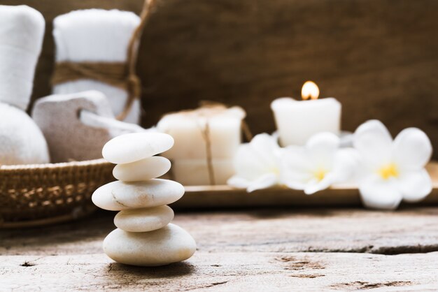 White zen stones and spa and treatment settting with towels, scrub, coconut soap and frangipani flowers on rustic wooden background