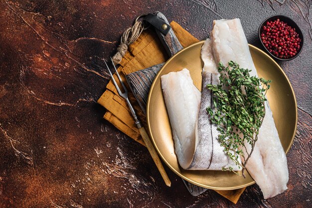 Whitefish fillet raw Haddock fish on plate with rosemary and thyme Dark background Top view Copy space