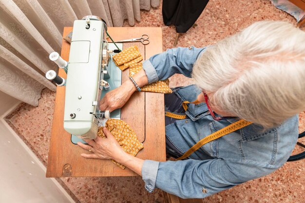 Whitehaired older woman sewing an orange retqal in front of an antique sewing machine