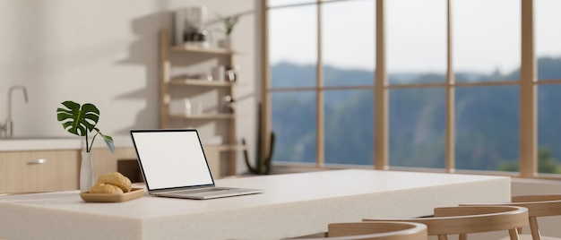 Макет ноутбука с белым экраном на белом обеденном столе в современной минималистической кухне. Домашнее рабочее пространство.