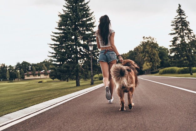 Photo who is coming first? full length rear view of young woman running with her dog through the park while spending time outdoors