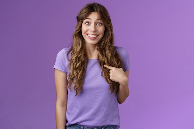 Who me awesome. Surprised silly tender delighted happy girl smiling impressed amazed pointing herself raise eyebrows astonished not expect hear own name stand purple background winning event