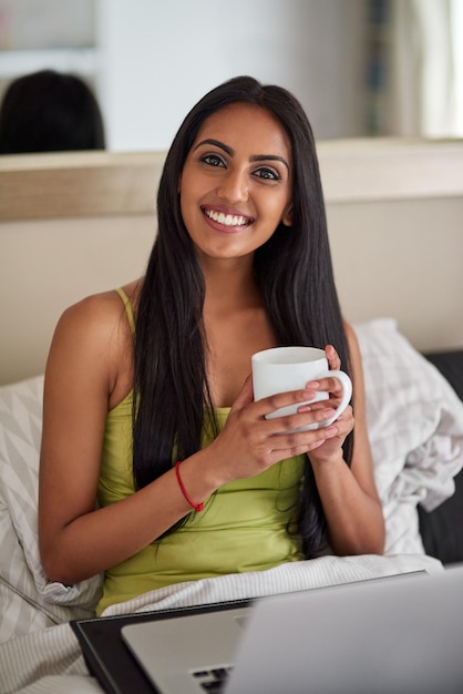 Who needs to leave the bed with high speed internet Shot of a relaxed young woman using a laptop and drinking coffee in bed