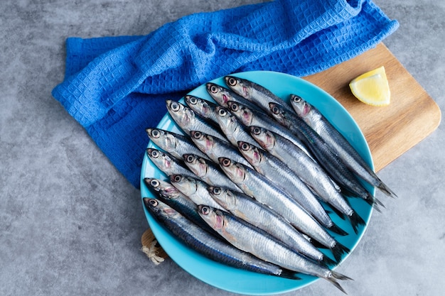 Whole anchovies on blue plate on marble background. Copy space. Fresh fish concept. Top view.