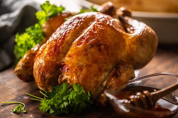 Whole baked chicken with crusty skin glazed with honey on top and parsley on the side.