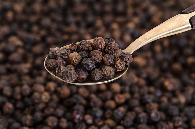 Photo whole black pepper on old spoon