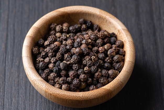 Whole black pepper in a small wooden bowl