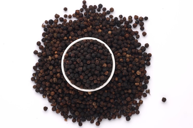 Whole black pepper  spices arranged in a white ceramic  bowl with white textured background