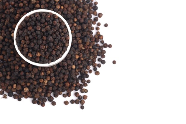 Whole black pepper  spices arranged in a white ceramic  bowl with white textured background