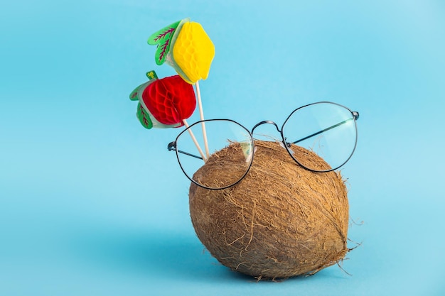 Photo whole brown coconut in shell in stylish glasses on bright blue background